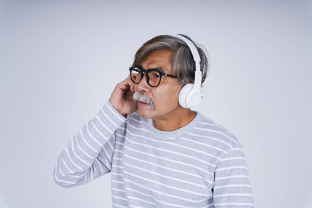 Retrato de anciano anciano anciano escuchando música con auriculares aislados sobre fondo blanco. - Foto, imagen