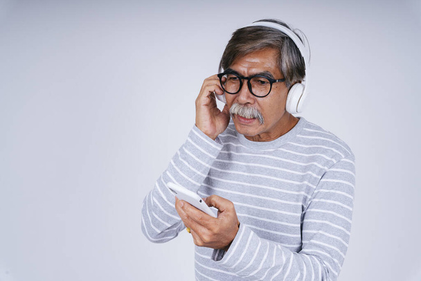Portré idős idős idős férfi hallgatni zenét vezeték nélküli fejhallgató és okostelefon izolátum fehér alapon. - Fotó, kép