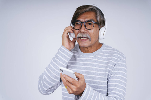 Muotokuva vanhusten vanhempi mies kuunnella musiikkia langattomalla kuulokkeella ja älypuhelin eristää valkoisella taustalla. - Valokuva, kuva