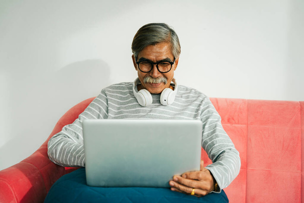 高齢者の男性は眼鏡を着用ソファの上に座っているラップトップコンピュータを使用して. - 写真・画像