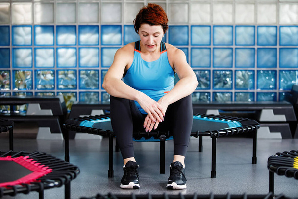 Mode de vie actif, forme physique. Adulte jolie femme fatiguée et assise sur un trampoline après un entraînement intense - Photo, image