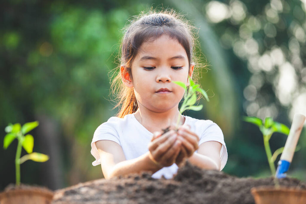 Söpö aasialainen lapsi tyttö tilalla nuori puu istutus musta maaperä puutarhassa hauskaa - Valokuva, kuva