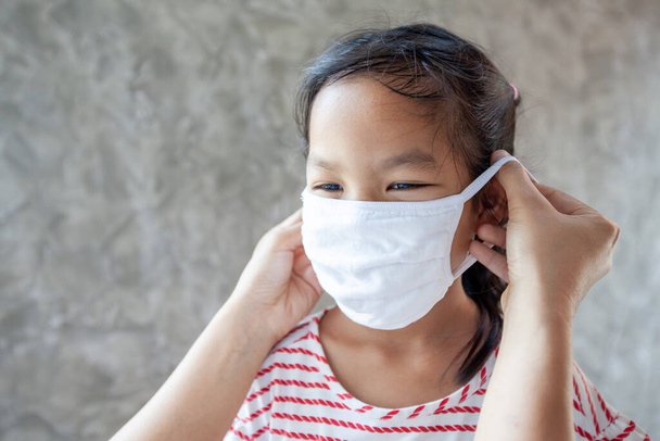 Aziatische moeder helpen haar dochter dragen bescherming masker om de coronavirus Covid-19 uitbraak situatie en luchtsmog vervuiling met PM 2,5 beschermen - Foto, afbeelding