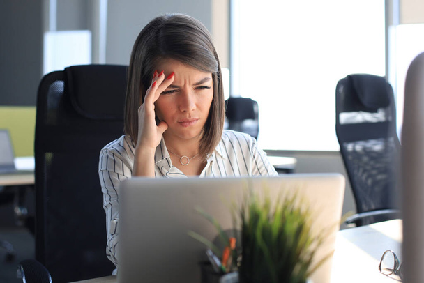 Frustrated business woman looking exhausted while sitting at her working place - Foto, Imagem