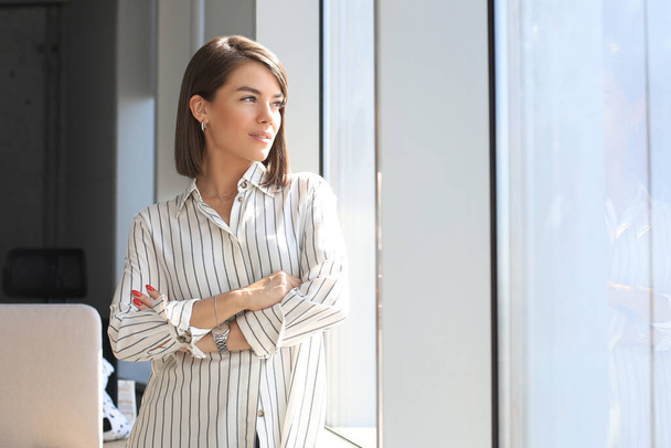 Attractive business woman in smart casual wear looking away and smiling while standing in the office. - 写真・画像