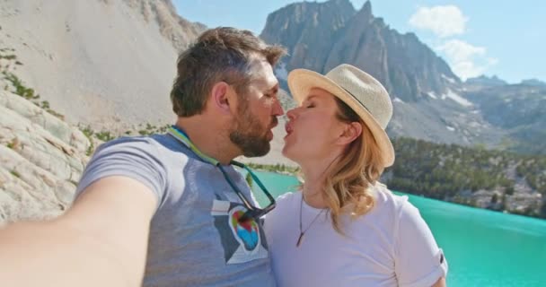 Casal viajante tira foto selfie no pico da montanha em belo lago azul, 4K - Filmagem, Vídeo