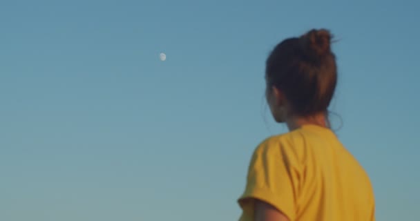 Verstoorde vrouw die naar de opkomende maan in de blauwe lucht kijkt. Achteraanzicht van meisje uit focus het observeren van aarde satelliet op zonnige dag handheld apparaat slow motion. Natuurlijke circadiaanse ritmes langzame levende levensstijl - Video
