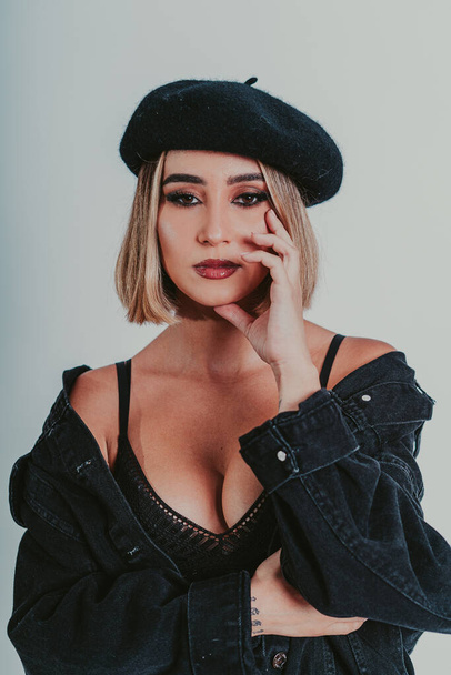 A portrait of a blonde female wearing a beret and a black denim jacket against a gray background - Foto, afbeelding