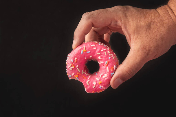 A closeup shot of a person holding a pink donut on a black background - Foto, Imagem