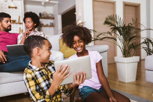 Niño y niña afroamericanos tumbados en el suelo y utilizando tableta digital. Familia en casa. - Foto, Imagen