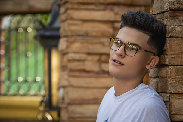 A closeup portrait of a handsome young man with a trendy hairstyle and sunglasses leaning on a stone wall - Foto, afbeelding