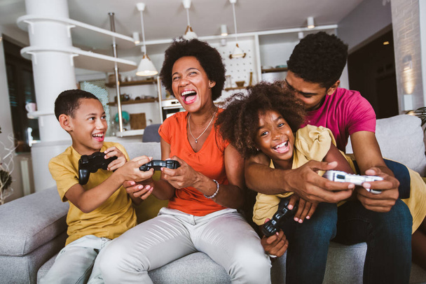 Famiglia afroamericana a casa seduta sul divano e a giocare ai videogiochi insieme - Foto, immagini