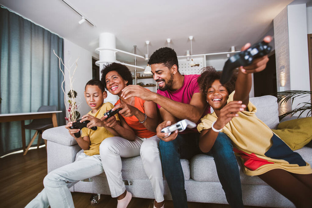 Afroamerykanska rodzina w domu siedzi na kanapie i gra w gry wideo razem - Zdjęcie, obraz