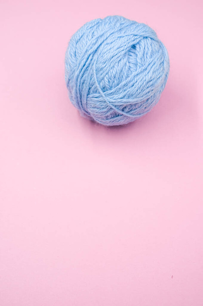 A vertical shot of a ball of blue yarn on a pink surface - Foto, afbeelding