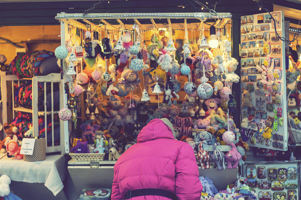 Kobieta wybierająca zabawki na świątecznym targu. Kobieta wybiera pamiątki na świątecznym targu. widok z tyłu. stonowana. - Zdjęcie, obraz