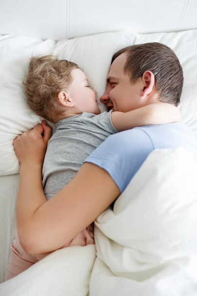 Семья, любовь, счастье и паранойя - вид сверху на счастливого отца и симпатичную маленькую дочку, веселящихся в постели - Фото, изображение