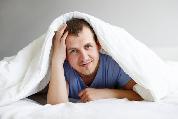 πορτρέτο του όμορφου άντρα ξαπλωμένος στο κρεβάτι κάτω από κουβέρτα - Φωτογραφία, εικόνα