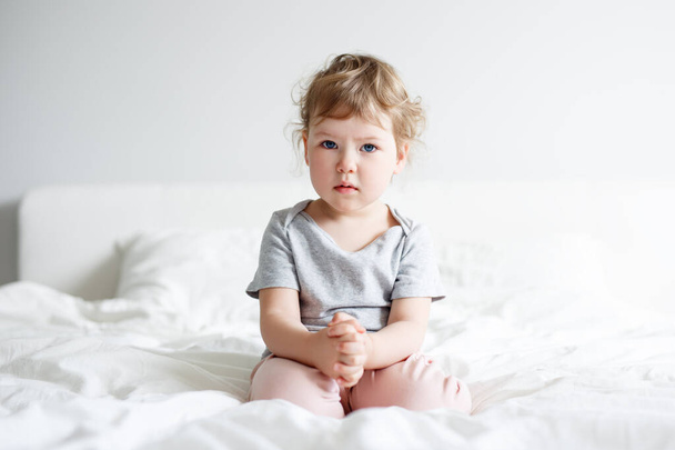 childhood and sadness concept - portrait of sad cute little girl sitting on bed - Fotó, kép