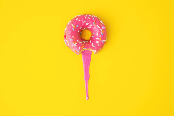 A high angle shot of a pink donut on a yellow surface - 写真・画像