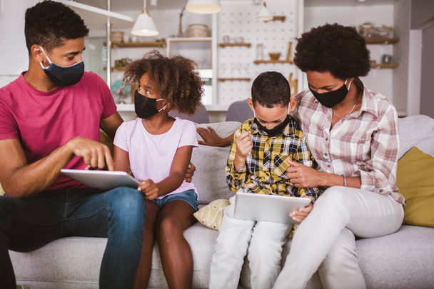 Сім'я вдома. Африканська американська сім'я в захисних масках з використанням цифрового планшета вдома.. - Фото, зображення