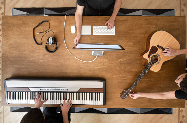 Музикант створює музику у своїй студії, граючи на музичній клавіатурі та акустичній гітарі. Процес роботи над звуком на фоні дерев'яної таблиці копіювання простору
 - Фото, зображення