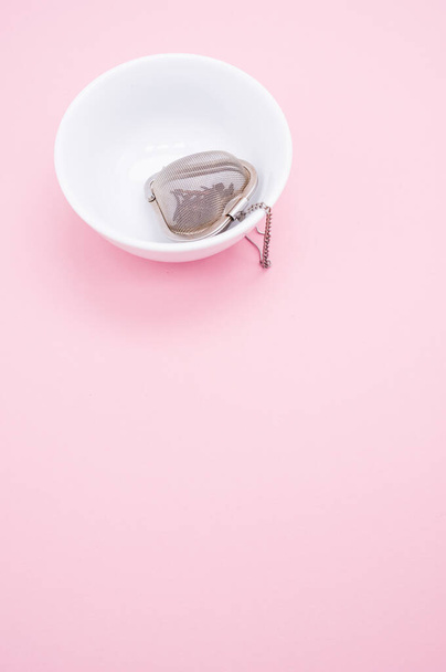 A closeup shot of a metal heart-shaped tea infuser in a bowl on a pink surface - Foto, Imagen