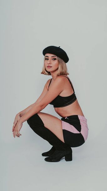 A vertical shot of a blonde female wearing a skirt paired with heeled boots and a beret against a gray background - Φωτογραφία, εικόνα