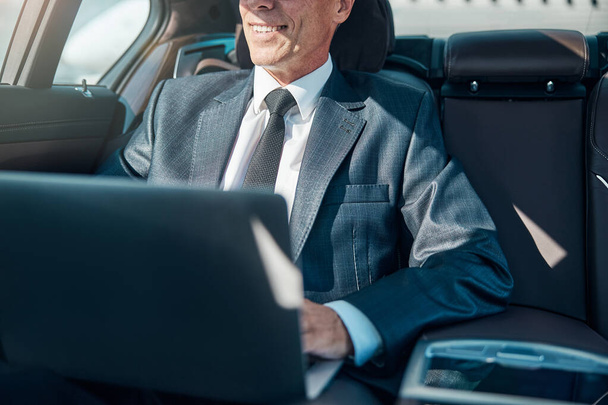 Homme élégant joyeux avec ordinateur portable en voiture - Photo, image