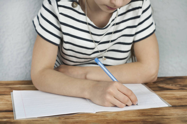 Dziewczyna w wieku 8-10 lat siedząca przy stole odrabia pracę domową. Szkolenie - Zdjęcie, obraz