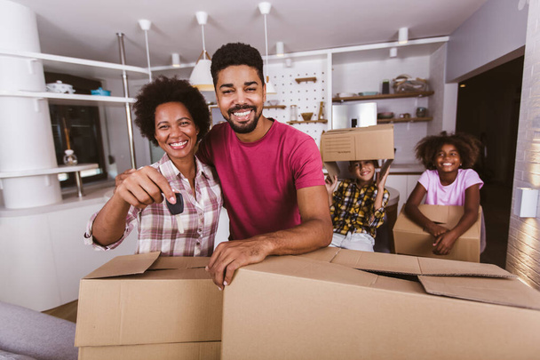 Familia sonriente llevando cajas en un nuevo hogar en el día de mudanza, sosteniendo llaves en un nuevo apartamento. - Foto, Imagen