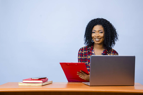 A pretty Afro-American female sitting in front of a laptop with a folder in her hands and working - Foto, immagini
