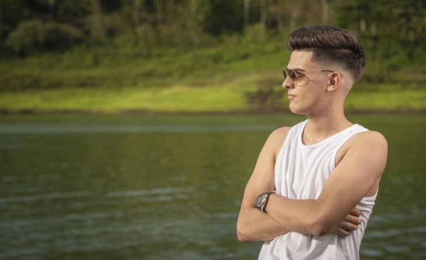 A closeup portrait of a confident young man with sunglasses standing with his arms crossed - 写真・画像