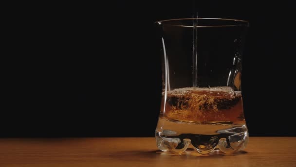 alkohol lub whisky wlewa kieliszek na czarnym tle - Materiał filmowy, wideo