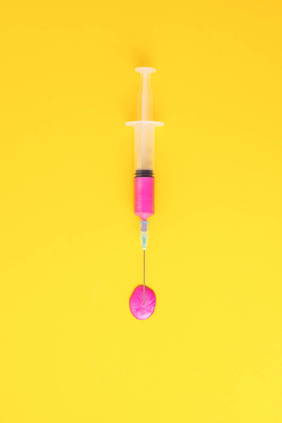 Plan vertical d'une seringue remplie d'un liquide rose sur une surface jaune - Photo, image