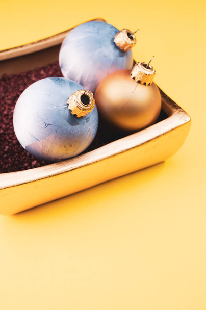 A vertical shot of Christmas ornaments in a luxurious bowl filled with small red rocks on yellow background - Foto, immagini