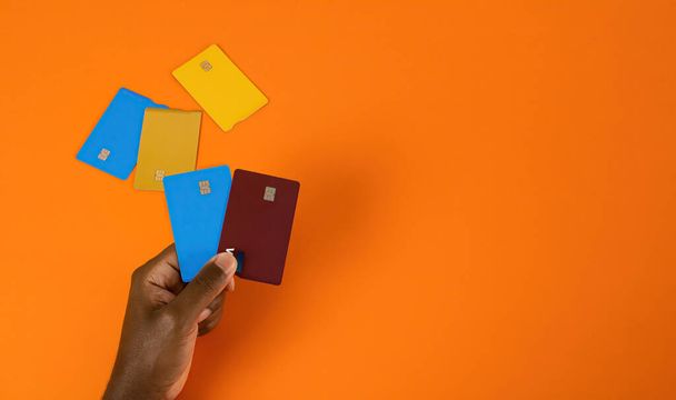 A top view of a person holding colorful credit cards against an orange background - Фото, изображение