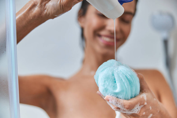 Alegre joven mujer verter gel de ducha en el baño loofah - Foto, imagen