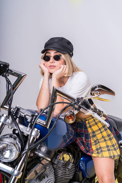 A portrait of a confident female wearing a skirt paired with a white t-shirt and posing on her motorcycle - Foto, Bild