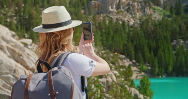 Mujer viajero toma fotos en el teléfono inteligente del lago verde cinematográfico. Aventura - Metraje, vídeo