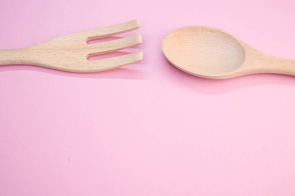 A high angle shot of a wooden spoon and fork on a pink surface - Foto, imagen