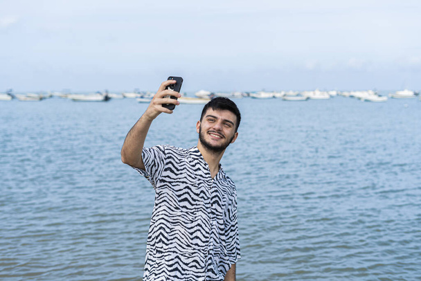 A Hispanic man taking selfies at a beach - Foto, immagini