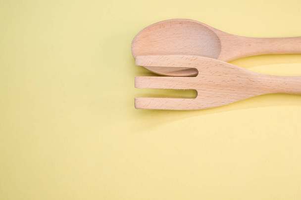 A high angle shot of a wooden spoon and fork on a yellow surface - 写真・画像