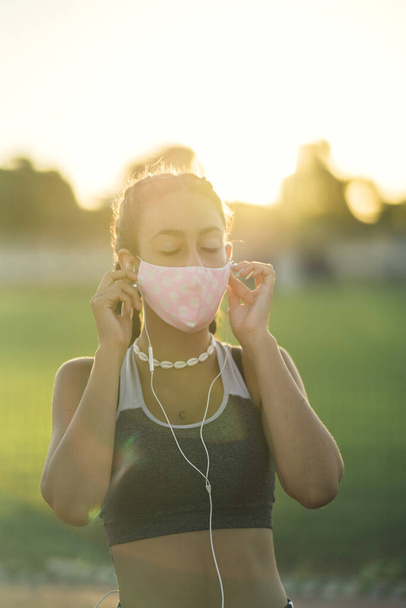 A shallow focus of a young female in sportswear with a facemask exercising at a park under the sunlight - Fotoğraf, Görsel
