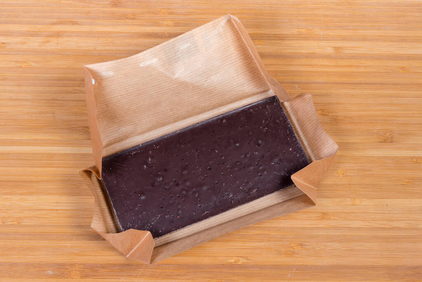 Barre de chocolat noir en papier ouvert sur la surface en bois, vue de dessus - Photo, image