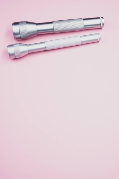 Two silver flashlights on a light pink background - Фото, зображення