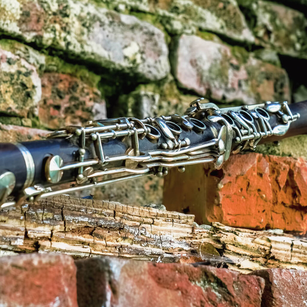 Fragment of an old and dirty magic clarinet on a background of a beautiful old broken brick wall as symbol of beautiful classical music - Photo, Image