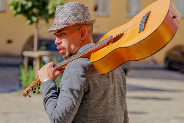 Back view of street musician wearing in titfer walking with a guitar on his shoulder. Music, art, creativit, freedom concept. - Photo, Image