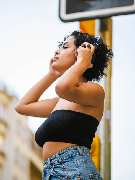 A vertical shot of a beautiful Brazilian female with headphones in the street - Zdjęcie, obraz
