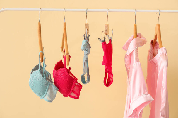 Σχάρα ρούχων με κομψά γυναικεία εσώρουχα και πιτζάμες στο φόντο χρώμα - Φωτογραφία, εικόνα