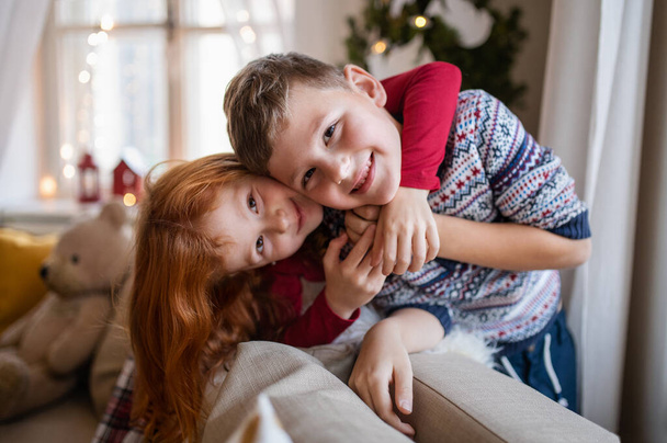 Small girl and boy indoors at home at Christmas, looking at camera. - Φωτογραφία, εικόνα
